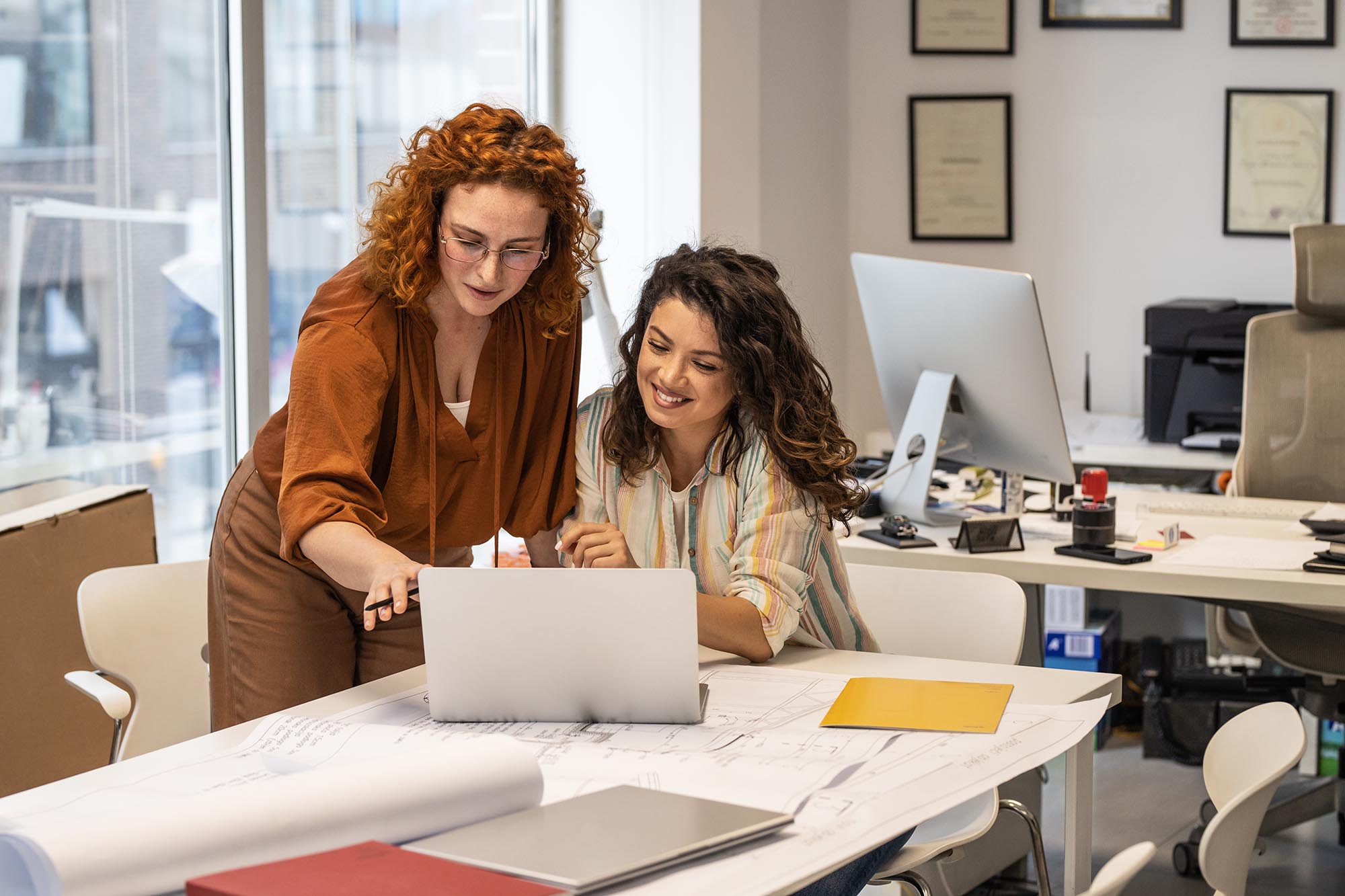 Two coworkers collaborating on account reconciliation software at laptop with financial documents
