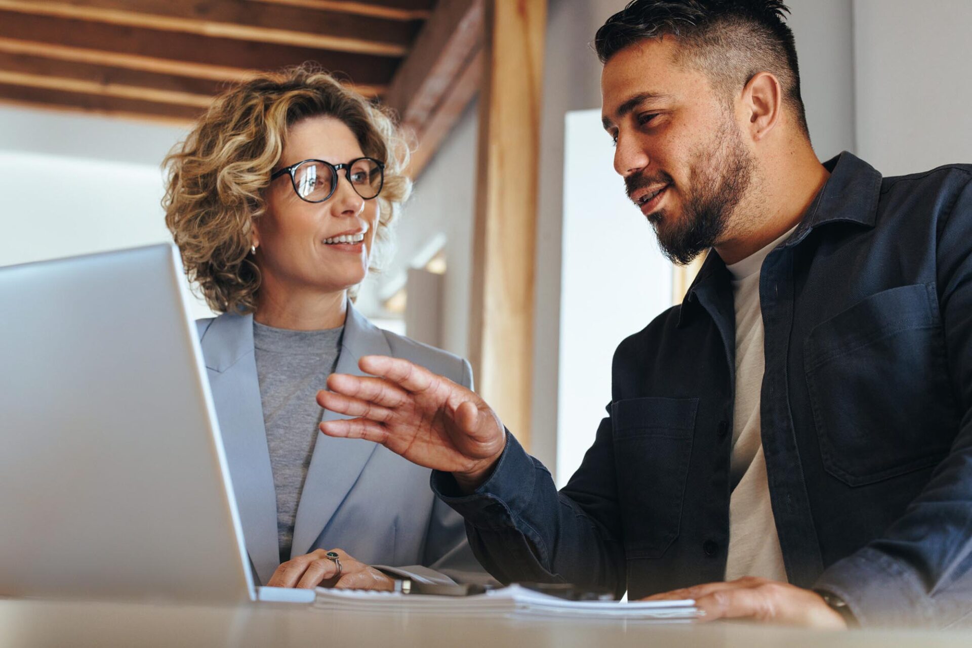 Two professionals discussing financial close management tasks while reviewing laptop in office