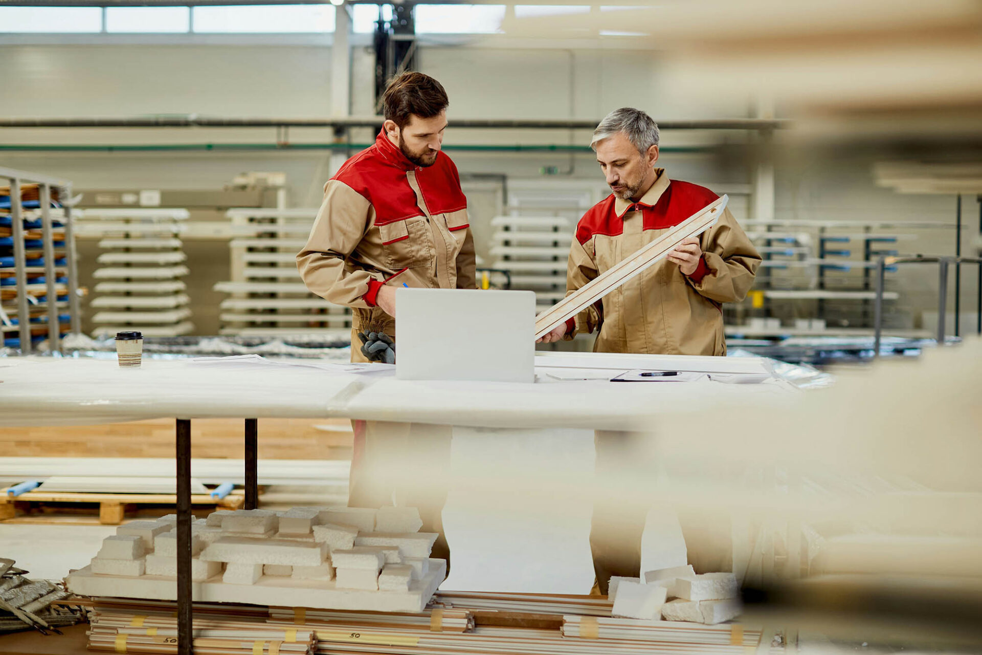 Industrial manufacturing professionals reviewing materials and using laptop for financial consolidation tasks